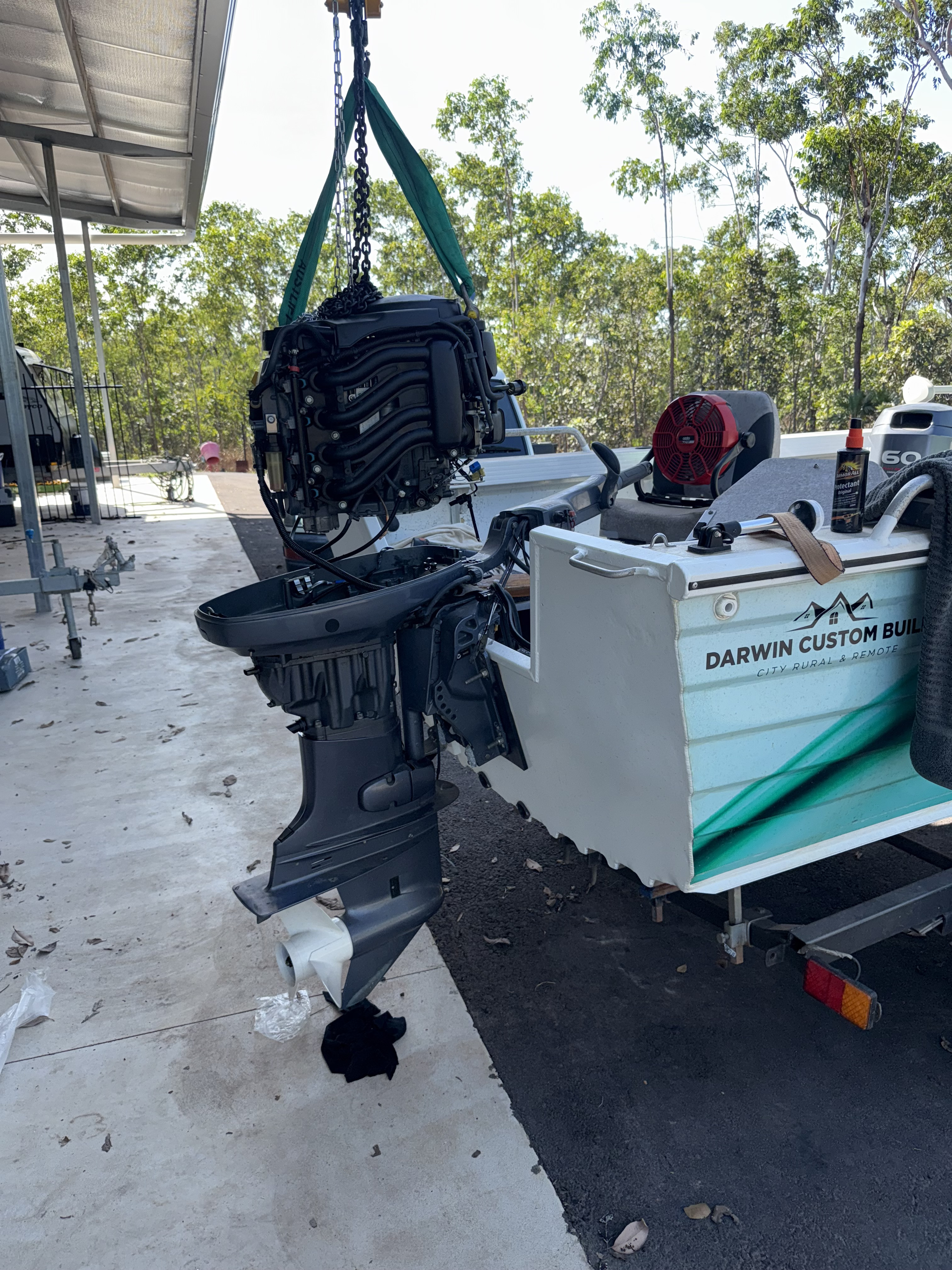 Marine mechanic repairing a large white outboard motor in a Darwin workshop